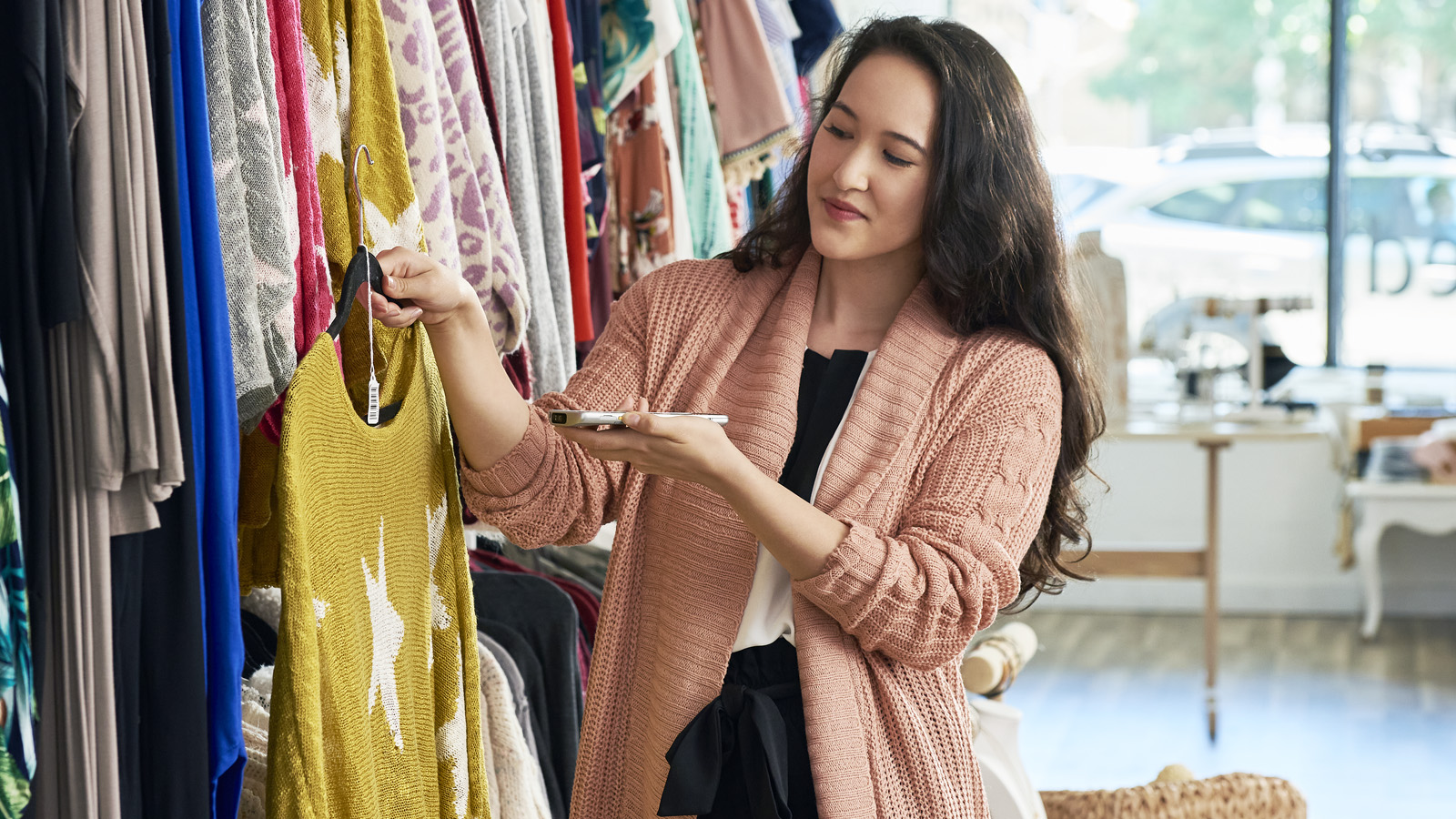 A woman in a clothing store holds a yellow sweater on a hanger while using a mobile computer to scan the garment’s tag, accessing its digital product passport (DPP).