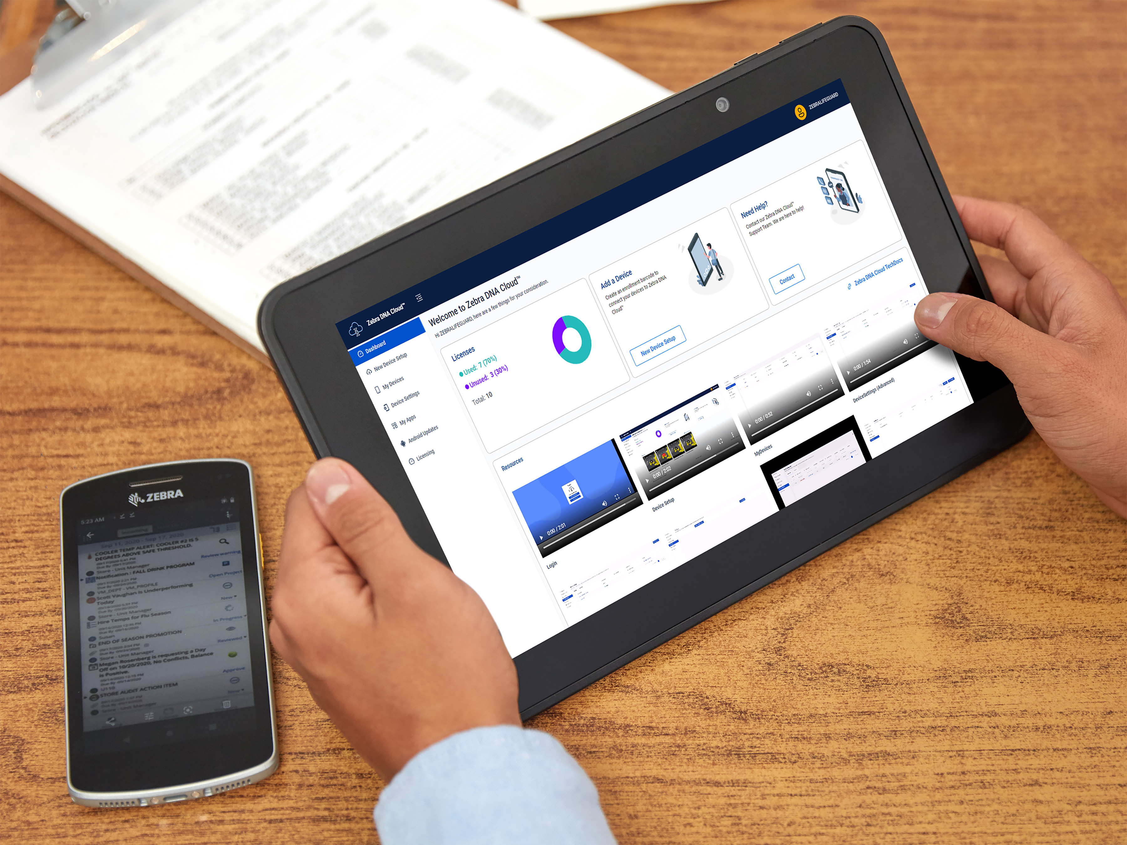 A person looks at a dashboard on their Zebra tablet while their Zebra handheld mobile computer sits next to them on the table