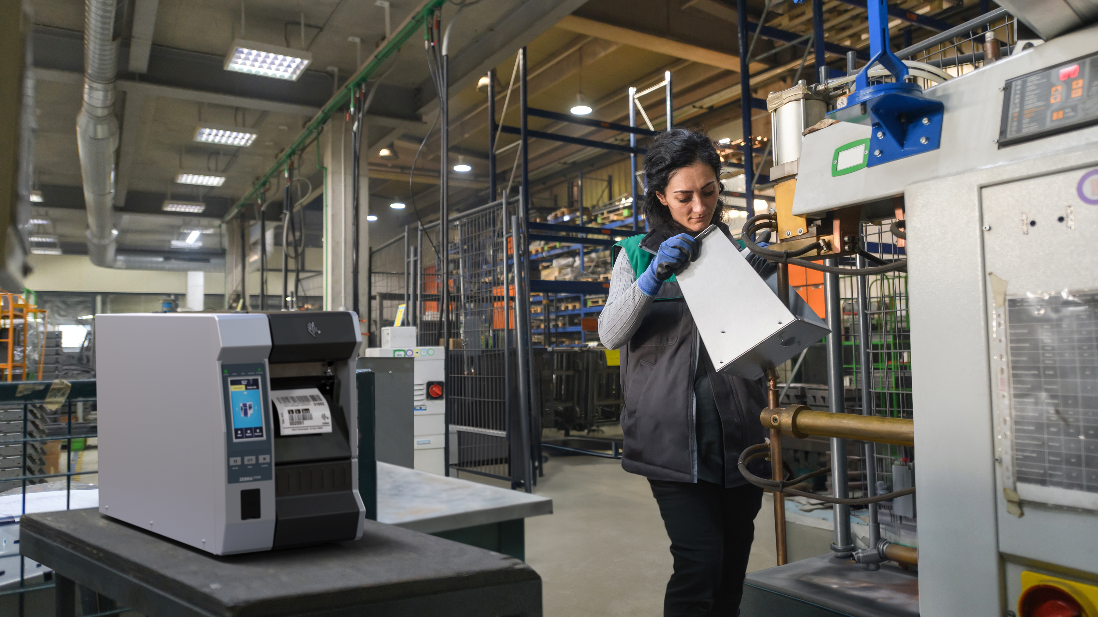 Worker in a manufacturing setting while a Zebra industrial printer prints a label.