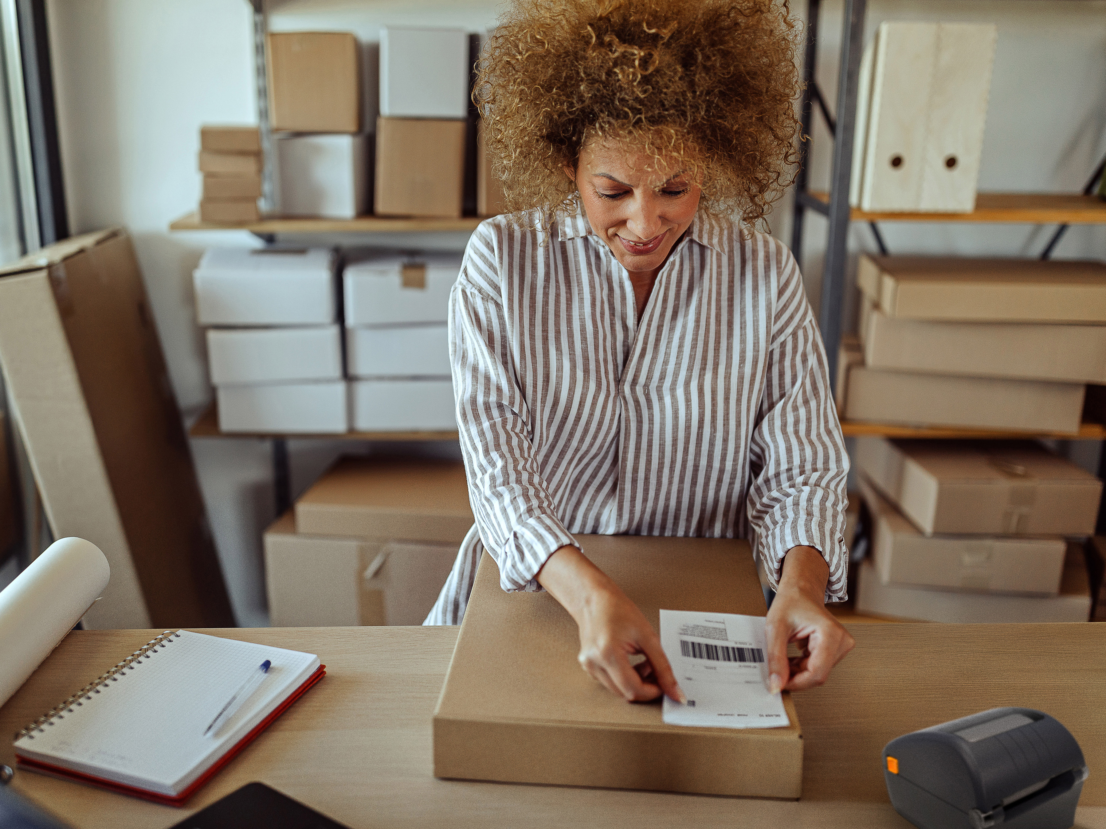 Female entrepreneur labeling delivery package with barcode at distribution warehouse