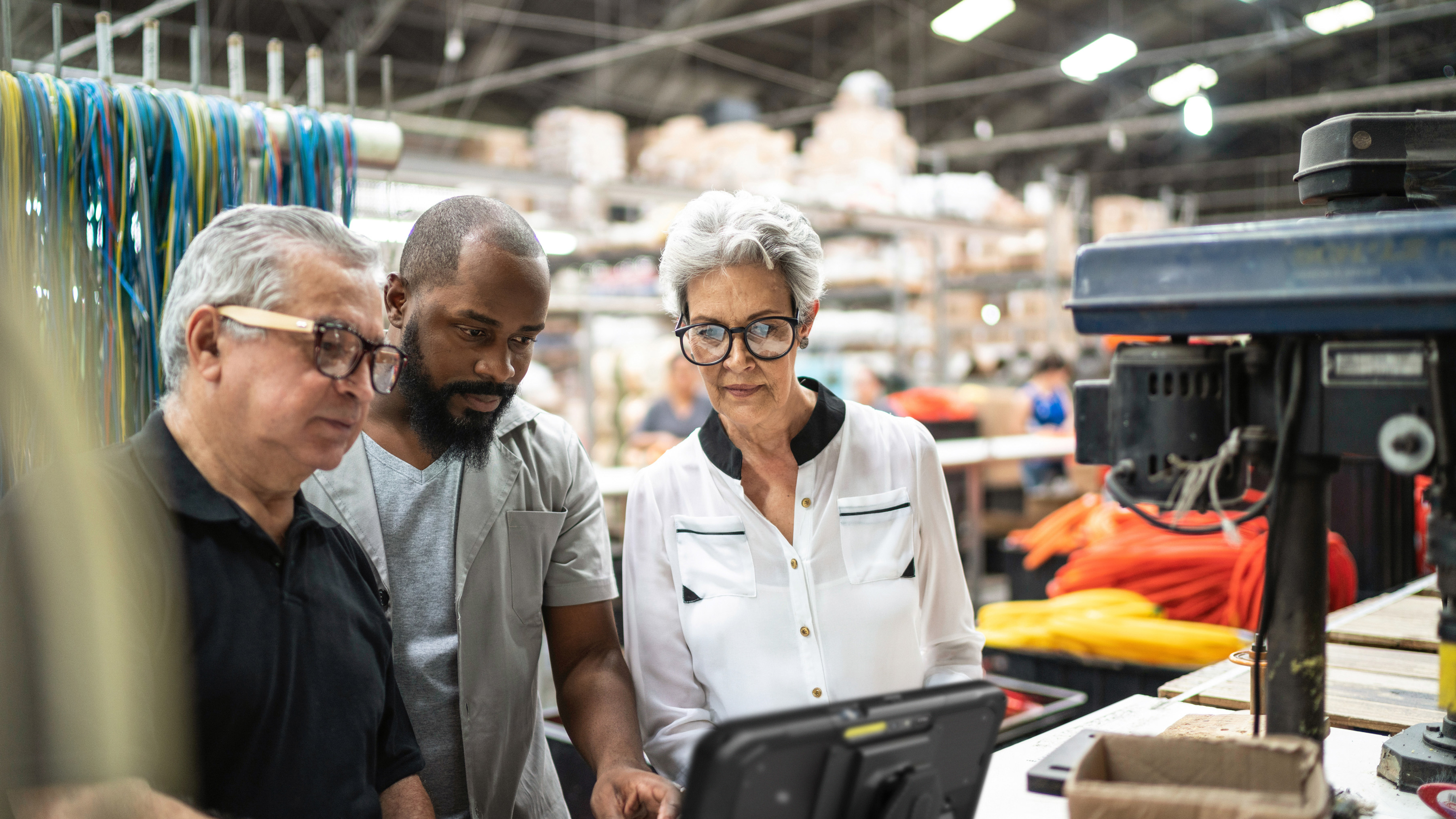 Three coworkers collaborating around a Zebra tablet inside of a factory setting.