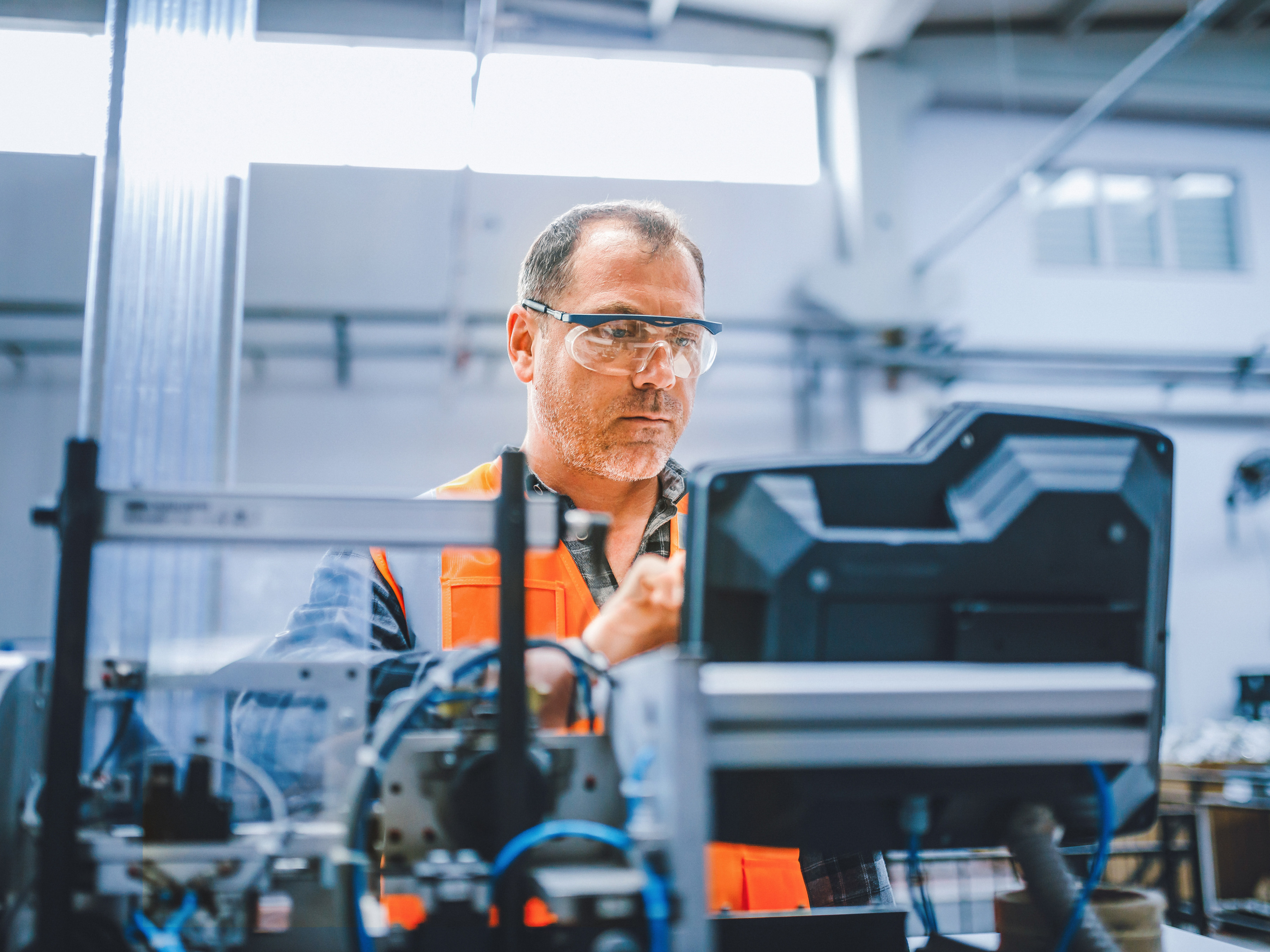 An industrial worker reviewing the controls on an equipment workstation inside of a factory.