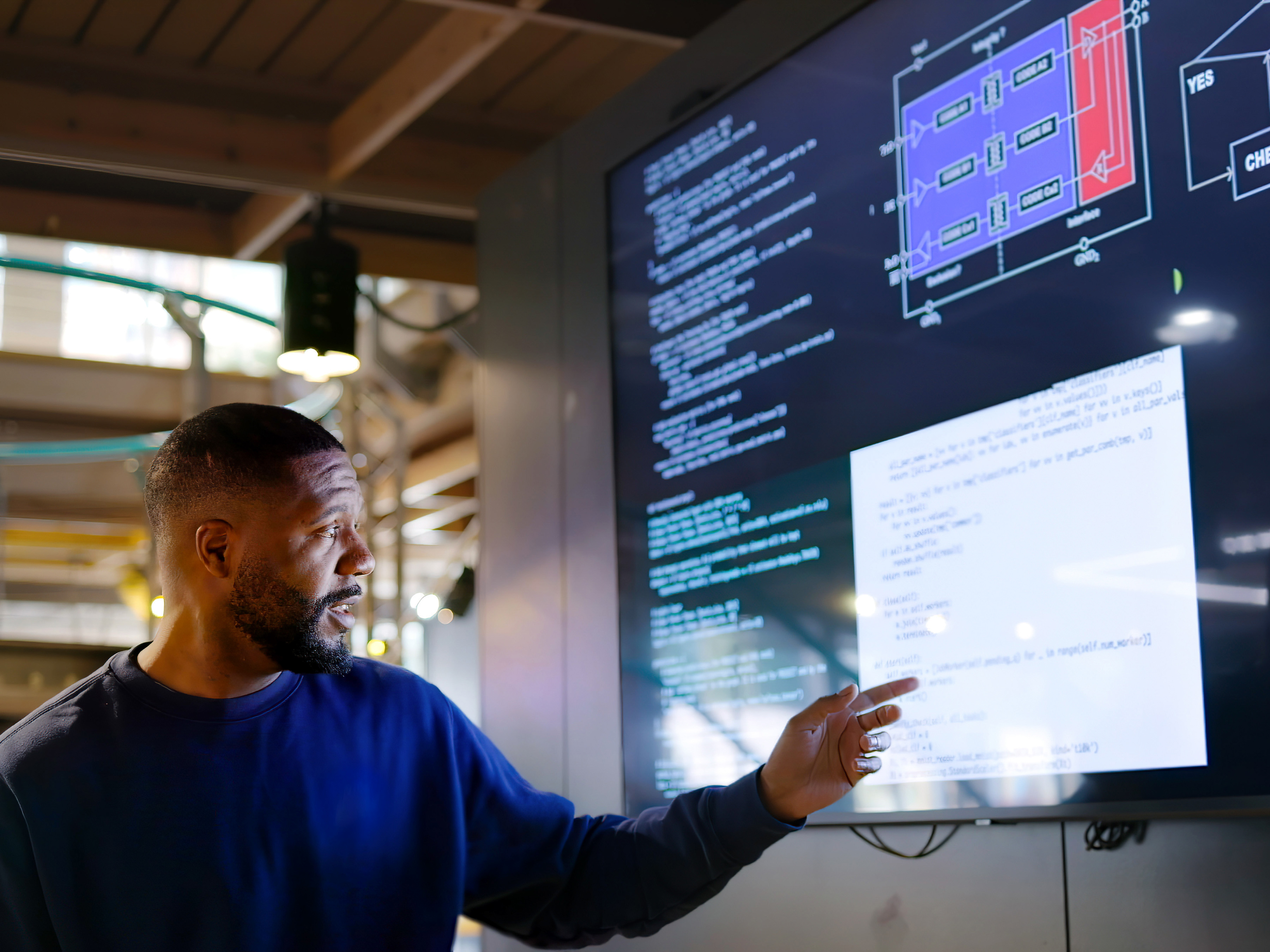 A person presenting code on a large monitor inside a modern office space.