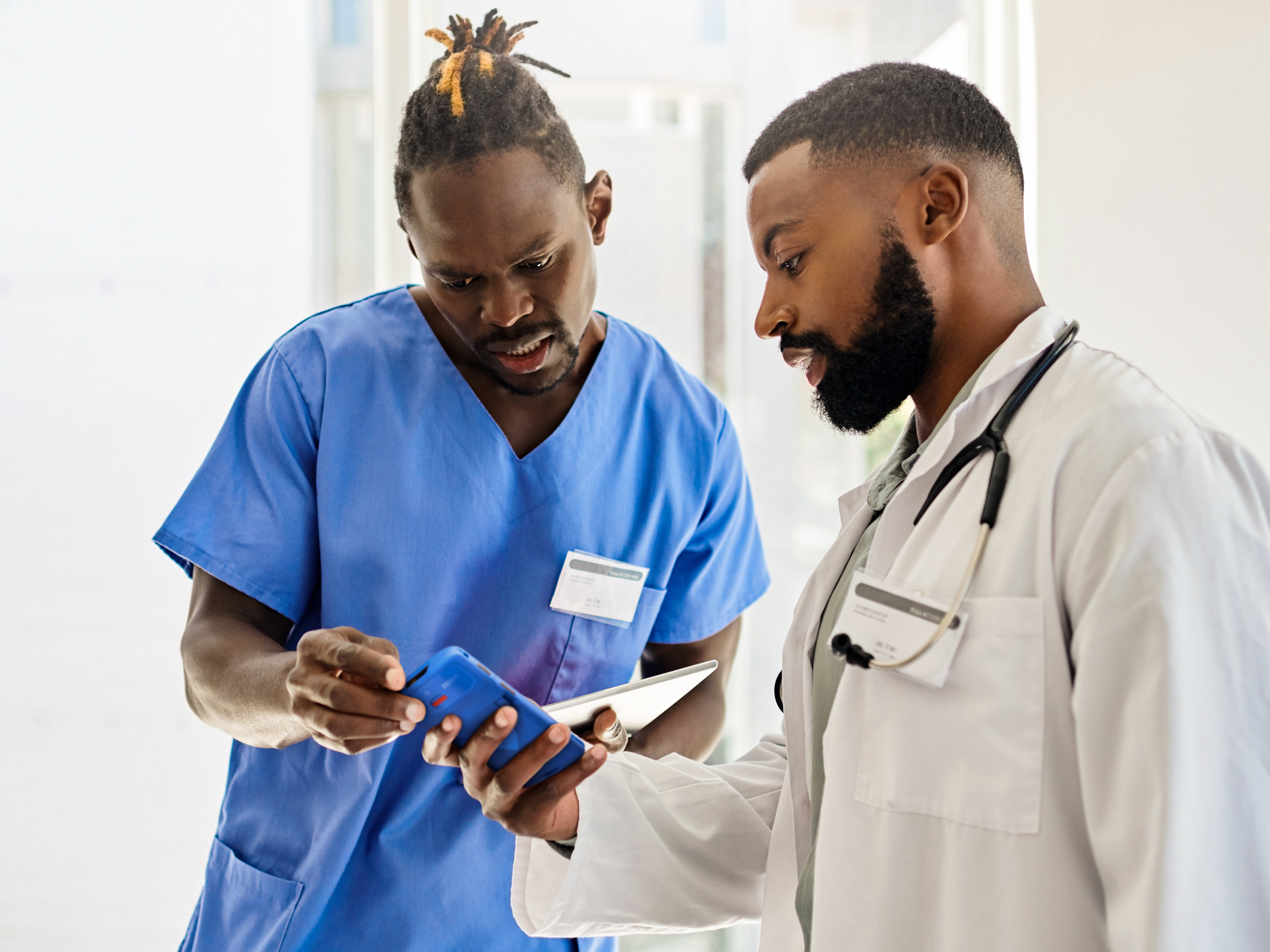 Two medical professionals reviewing a Zebra handheld mobile computer inside of a hospital.