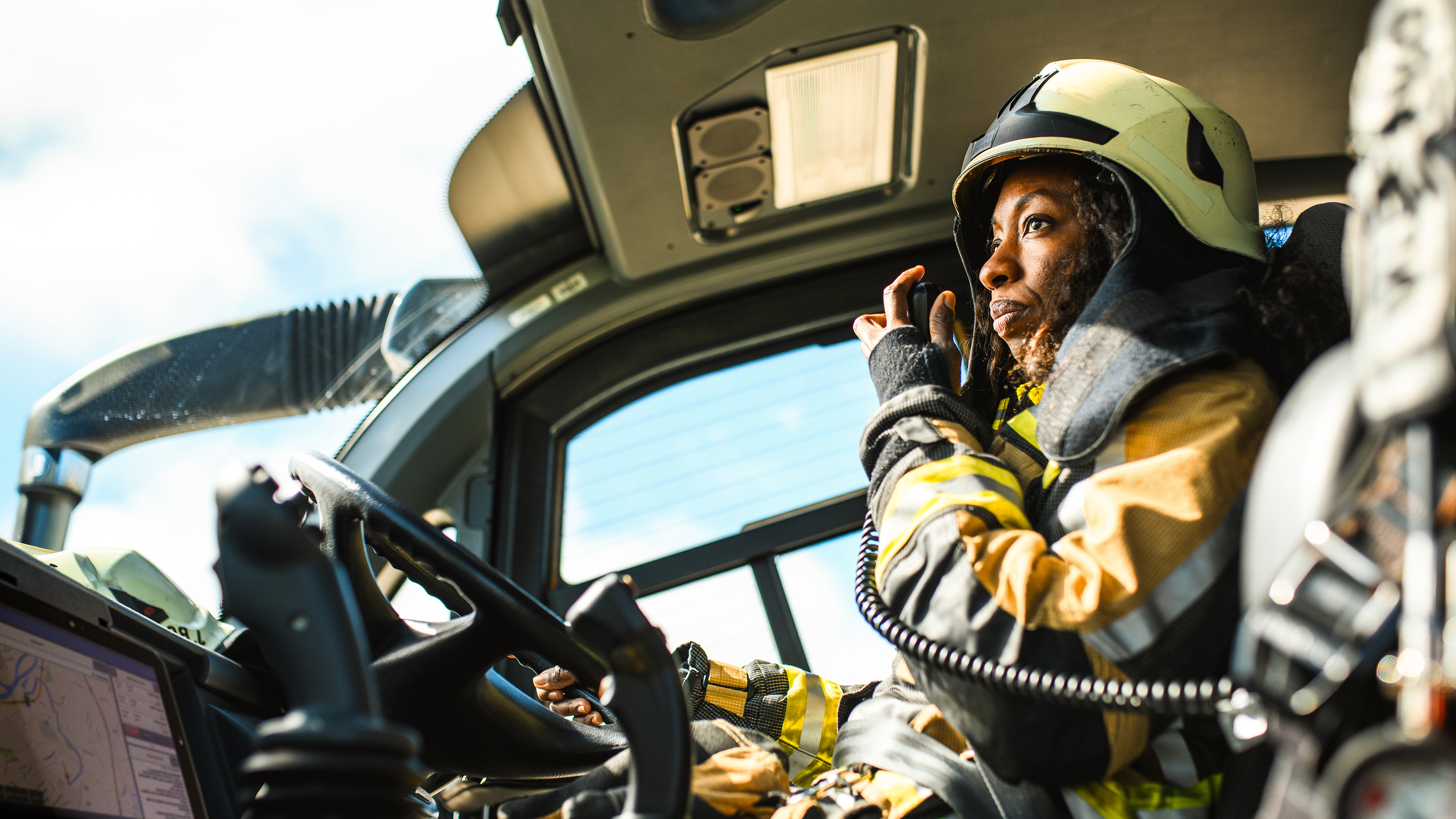 A firefighter talking on a walkie talkie with a Zebra rugged tablet while driving a firetruck.