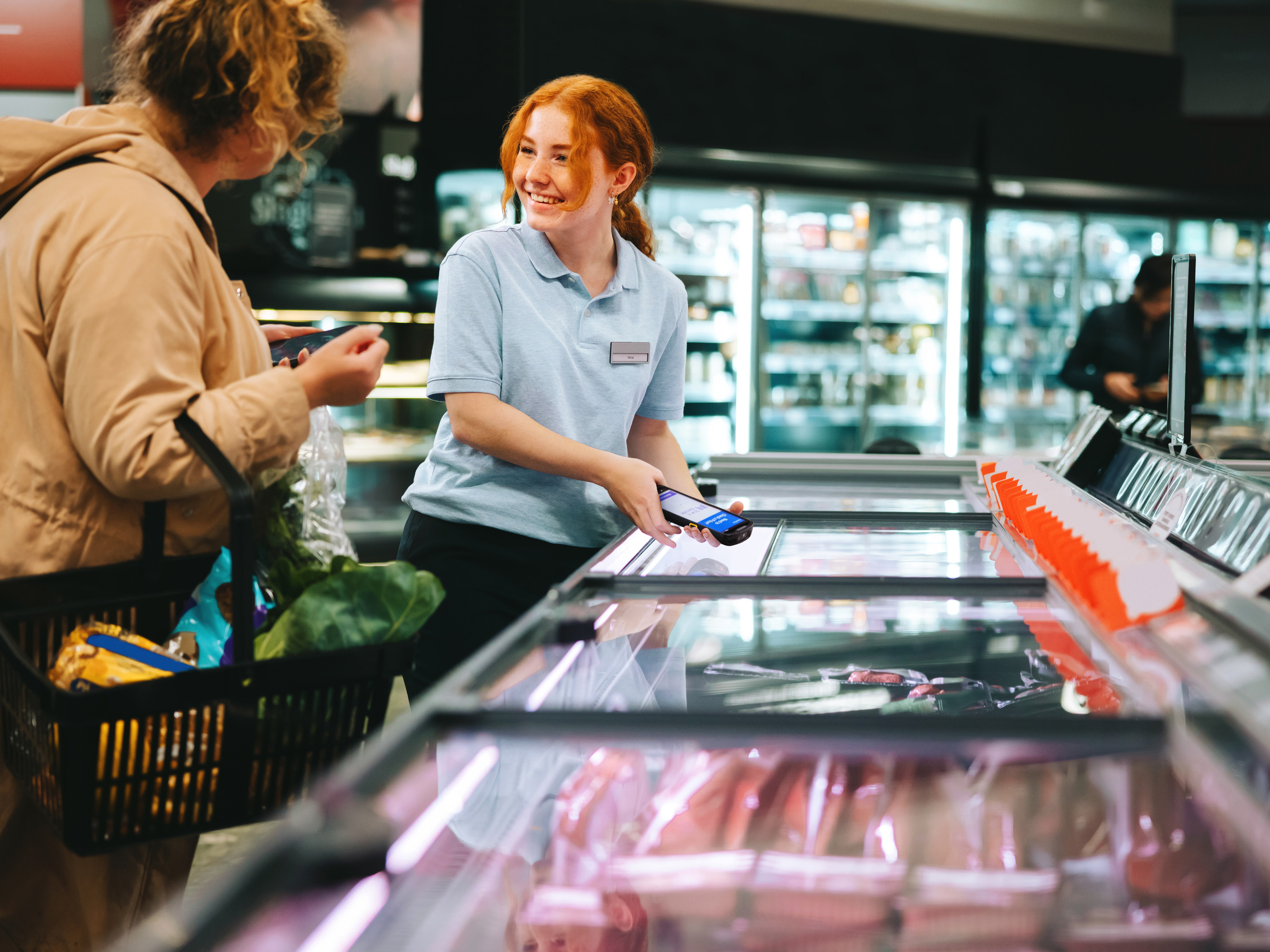 Retail employee with a Zebra handheld mobile computer assisting a customer in the meat department of a grocery store.