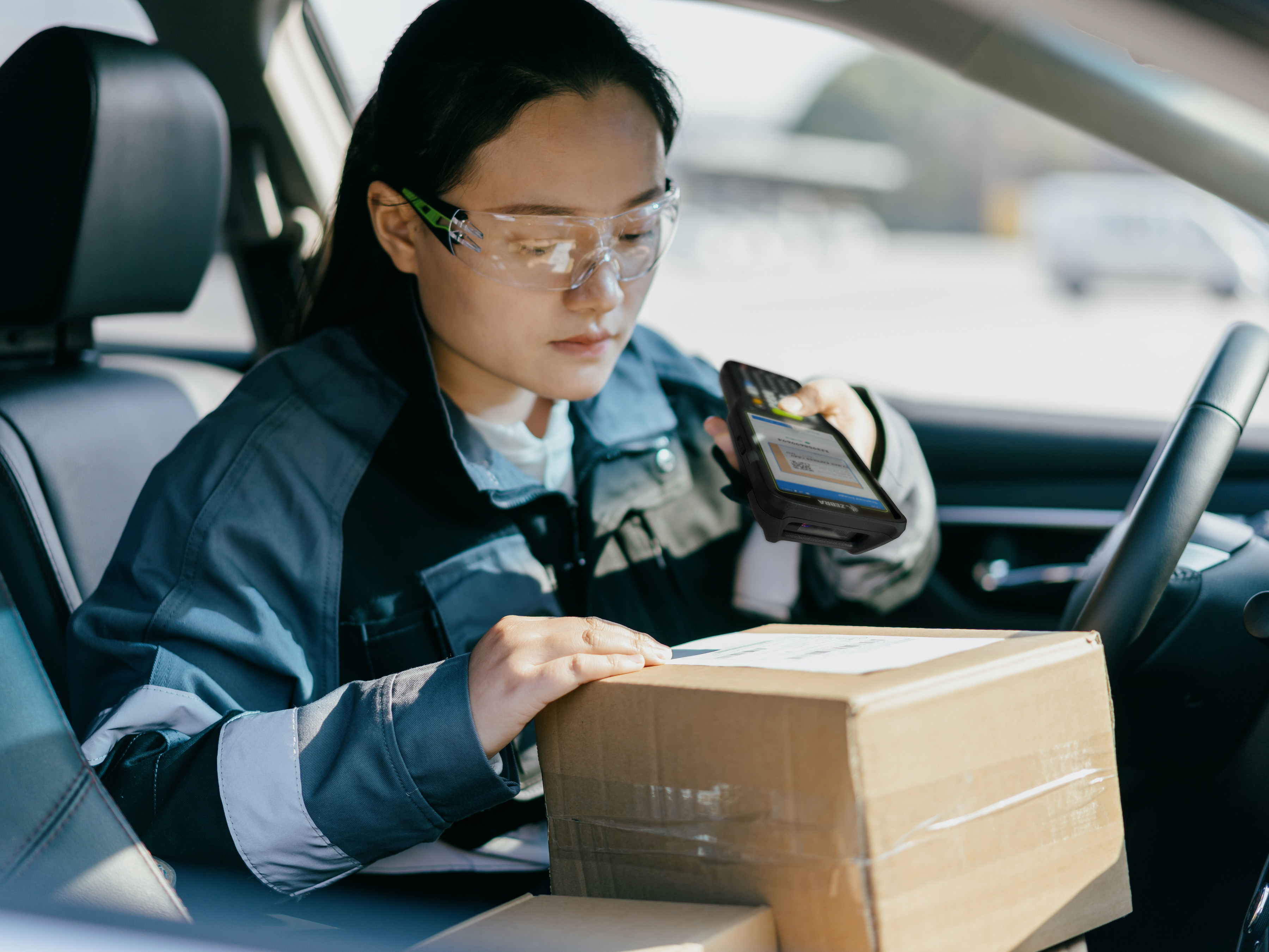 Courier in a delivery vehicle scanning a parcel with a Zebra handheld mobile computer.