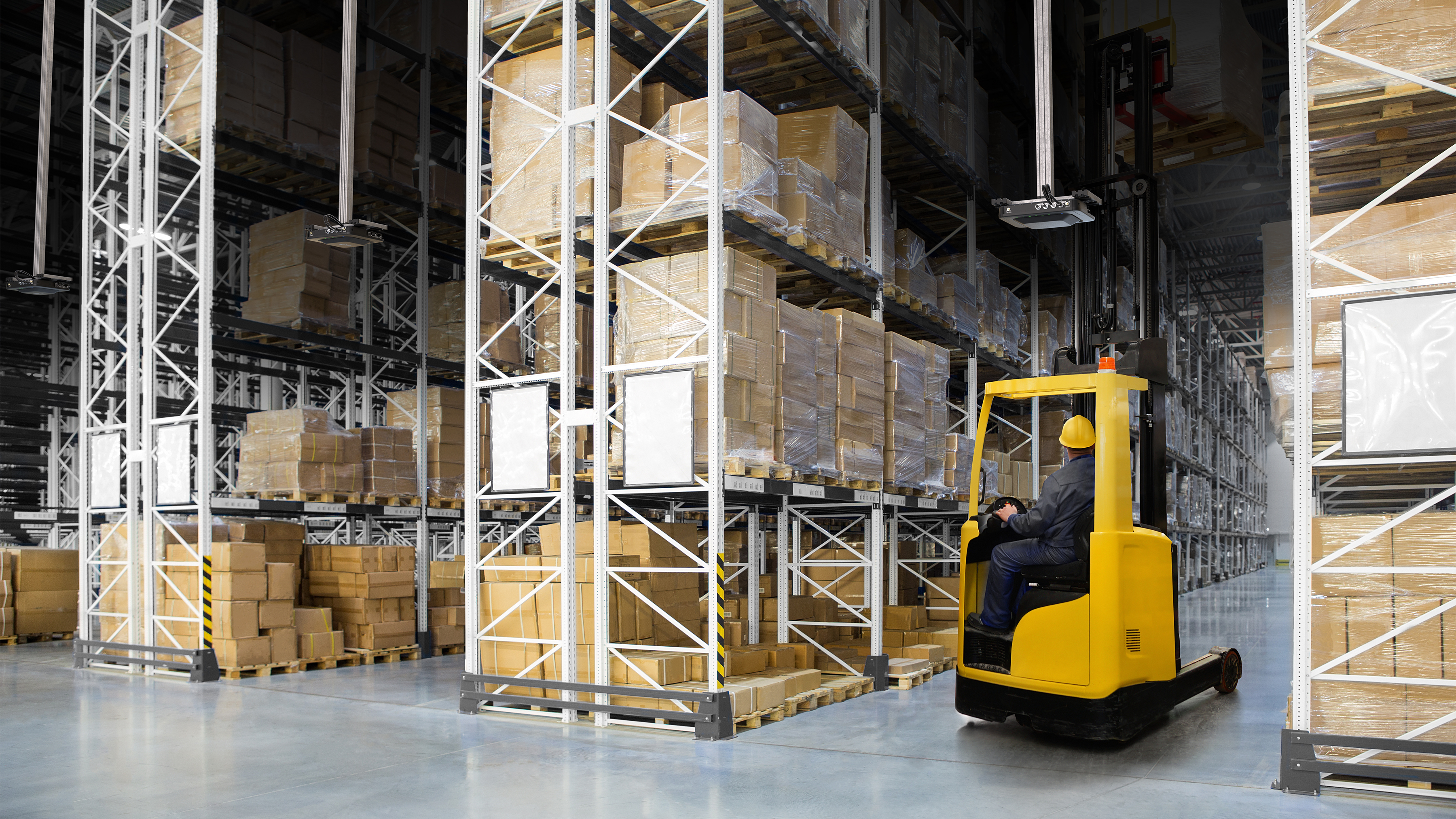 Worker on a small yellow forklift in a warehouse using the overhead Zebra FXR90 RFID reader to scan multiple barcodes at once in the aisle on many boxes.